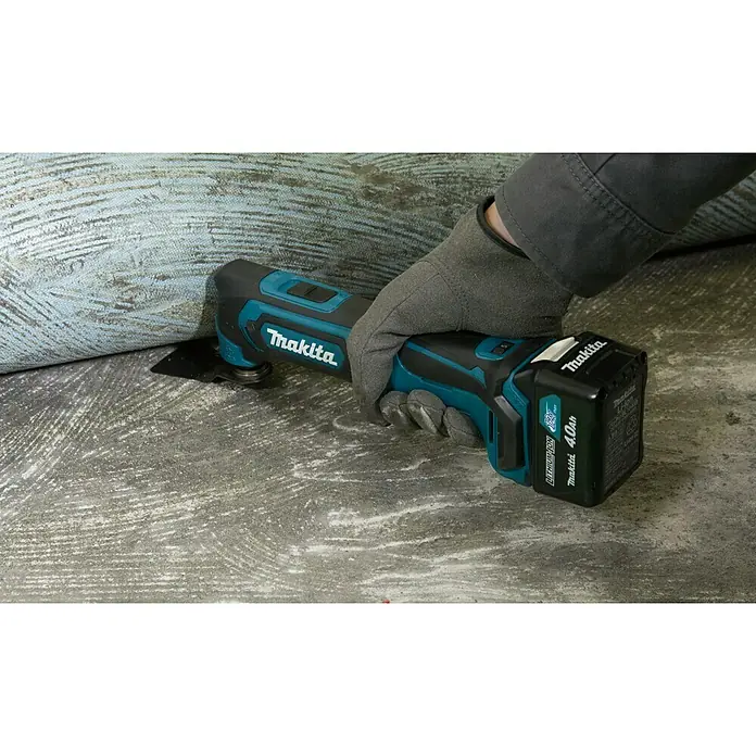 Makita CXT 12V max. Akku-Multifunktionswerkzeug TM30DZ - 12 V, Ohne Akku - Ein Akku-Multifunktionswerkzeug von Makita wird von einer Person mit Handschuhen auf einem gemusterten Untergrund gehalten.