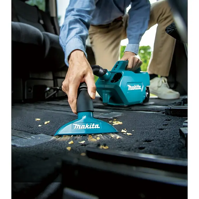 Makita LXT 18V Akku-Staubsauger DCL184Z - 18 V, Ohne Akku, Behältervolumen: 0,5 l - Ein Mann reinigt mit einem Makita Akku-Staubsauger den Innenraum eines Autos, der mit Krümeln übersät ist.