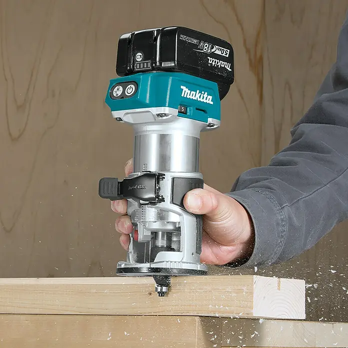 Makita LXT 18V Akku-Multifunktionsfräse DRT50ZJX2 - 18 V, Ohne Akku, Leerlaufdrehzahl: 10.000 U/min - 30.000 U/min - Nahaufnahme eines Makita Akku-Fräsers in Aktion, der Holz bearbeitet und Späne erzeugt. Der Fräser ist mit einem Akku ausgestattet.