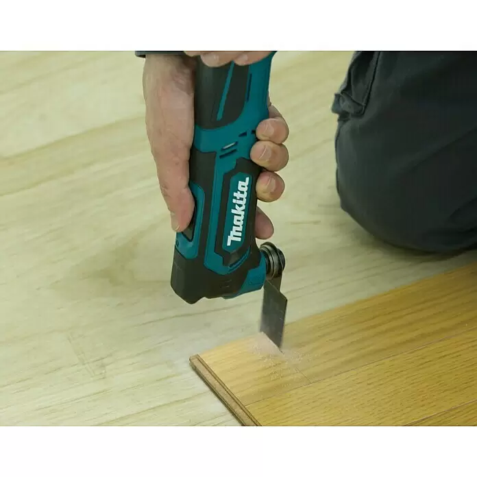 Makita CXT 12V max. Akku-Multifunktionswerkzeug TM30DZ - 12 V, Ohne Akku - Eine Hand hält ein türkis-schwarzes Makita Multifunktionswerkzeug, das ein Holzbrett schneidet und Sägemehl erzeugt.