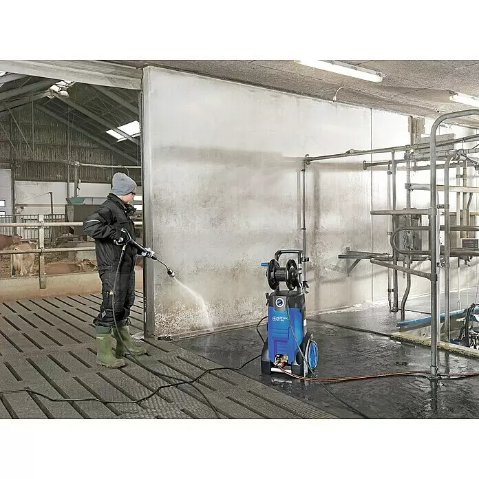 Nilfisk Hochdruckreiniger MC4M-160/620 XT - 3.000 W, Max. Druck: 160 bar, Fördermenge: 620 l/h - Eine Person reinigt mit blau-schwarzem Hochdruckreiniger eine Betonwand in einem Stallgebäude.