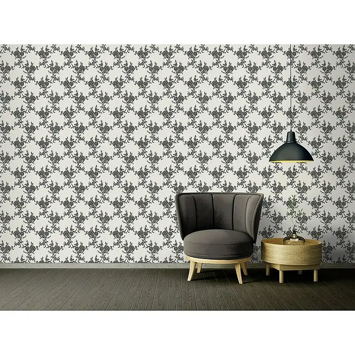 A.S. Création Vliestapete Blüten - Schwarz/Weiß, Floral, L x B: 10,05 x 0,53 m - Stilvoller grauer Sessel mit passendem Beistelltisch unter einer Pendelleuchte, vor einer floral gemusterten Wand.