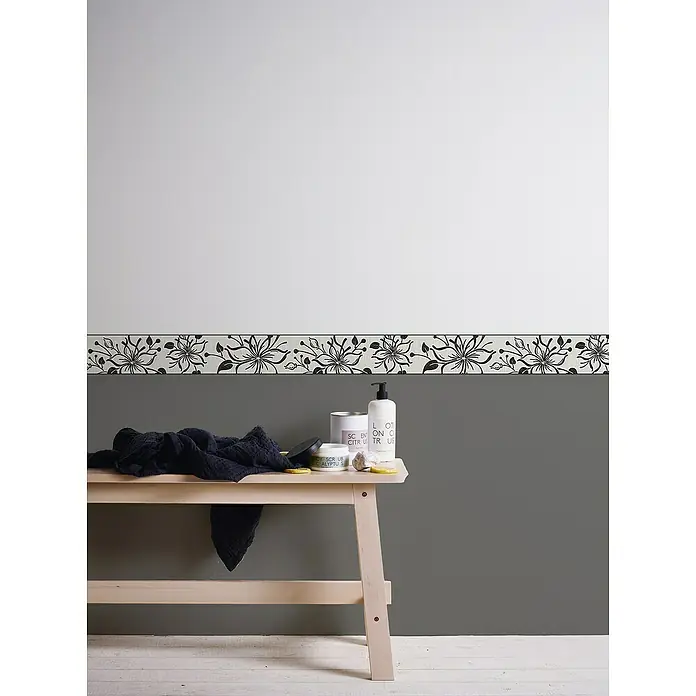 A.S. Création Only Borders 11 Tapetenborte Blume - Schwarz/Weiß, 5 x 0,13 m, Selbstklebefolie - Ein heller Holztisch mit einer Auswahl an Hautpflegeprodukten, darunter Lotionen und Peelings, vor einer zweifarbigen Wand mit floralem Muster.