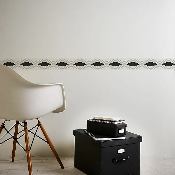 A.S. Création Only Borders 11 Tapetenborte Grafische Wellen - Kunststoff, Schwarz/Weiß - Nahaufnahme einer modernen Raumgestaltung mit einem dekorativen Wandbordüre, einem stilvollen Stuhl und schwarzen Aufbewahrungsboxen.