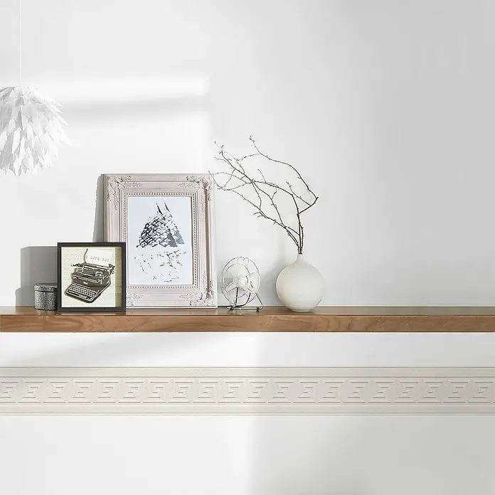 A.S. Création Only Borders Tapetenborte 6 - Kunststoff, Weiß - Eine Innenaufnahme mit einem Regal, auf dem Dekorationen wie Bilderrahmen und eine Vase mit Zweigen stehen, unterhalb ein weißes Zierband.
