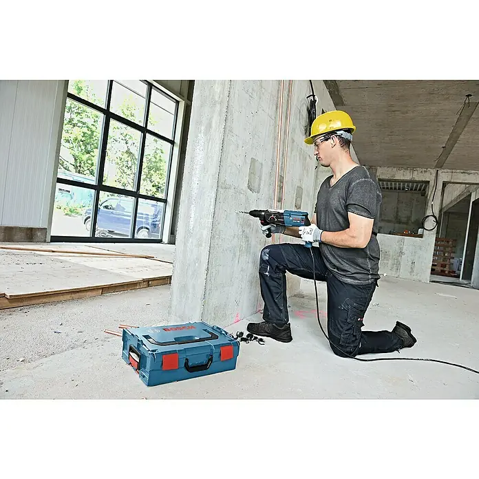 Bosch Professional Kombihammer GBH 2-28 F - 880 W, 3,2 J, SDS-Plus-Aufnahme, Ohne Bohrer & Meißel - Ein Bauarbeiter kniet mit einem Bosch-Bohrhammer vor einer Betonwand, während ein Bosch-Werkzeugkoffer im Vordergrund steht.