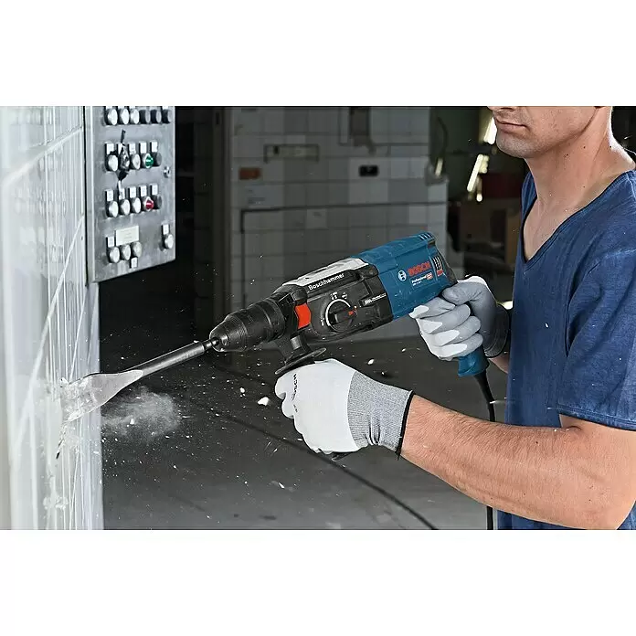Bosch Professional Kombihammer GBH 2-28 F - 880 W, 3,2 J, SDS-Plus-Aufnahme, Ohne Bohrer & Meißel - Ein Mann nutzt einen blau-schwarzen Bosch Professional Bohrhammer, um Fliesen von einer Wand zu schlagen, dabei entsteht Staub.