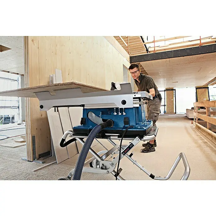 Bosch Professional Tischkreissäge GTS 10 XC - 2.000 W, Durchmesser Sägeblatt: 254 mm, Schnitttiefe bei 90 °: 79 mm - Ein Bauarbeiter benutzt eine Bosch Tischkreissäge mit Arbeitstisch in einem unfertigen Gebäude. Schutzausrüstung wird getragen.