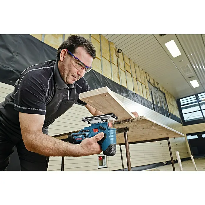 Bosch Professional Akku-Stichsäge GST 12V-70 - 12 V, 2 Akkus, 3 Ah, 1.500 /min - 2.800 /min - Mann schneidet Holz mit einer Bosch Stichsäge. Das blaue Werkzeug mit Akku ist für präzise Schnitte konzipiert und liegt gut in der Hand.