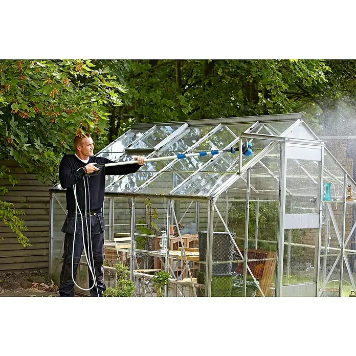 Nilfisk Boquilla telescópica para alturas - Zona de ajuste: 4,2 m, Específico para: Limpiadoras de alta presión Nilfisk - Un hombre limpia un invernadero con un cepillo telescópico, asegurando una luz solar óptima y el crecimiento de las plantas.