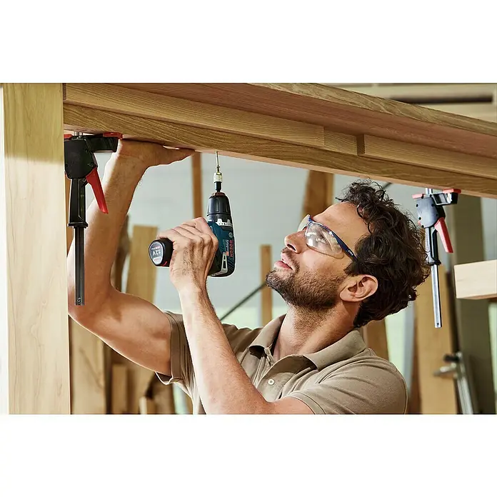 Bosch Professional Akku-Bohrschrauber GSR 12V-35 - 12 V, 2 Akkus, 3 Ah - Ein Mann benutzt einen Bosch Akku-Bohrschrauber, um ein Holzstück zu befestigen, während er eine Schutzbrille trägt, um seine Augen zu schützen.