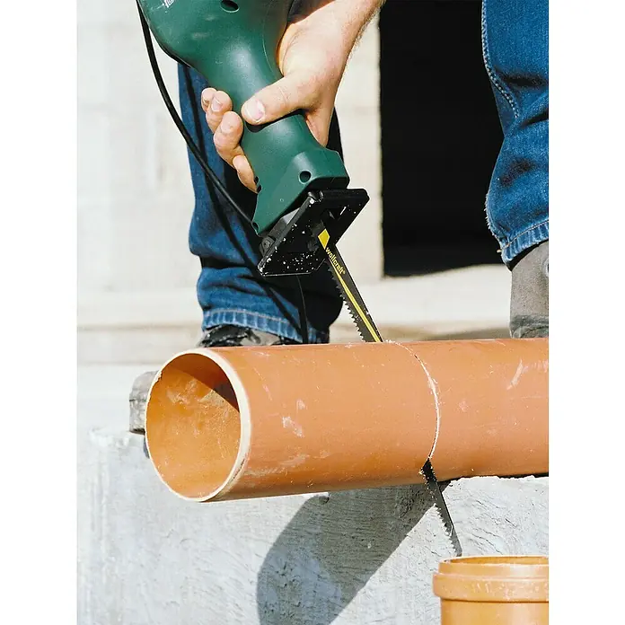 Wolfcraft Säbelsägeblatt - 2 -tlg., Länge: 300 mm - Eine grüne Säbelsäge von wolfcraft schneidet ein braunes Kunststoffrohr. Eine Person bedient die Säge.