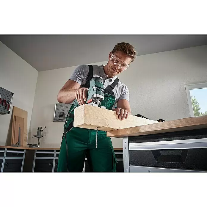 Wolfcraft Stichsägeblatt - Holz, T-Schaft, 2 Stk. - Mann sägt mit einer grün-schwarzen Stichsäge einen dicken Holzbalken auf einer Werkbank, trägt Schutzbrille.