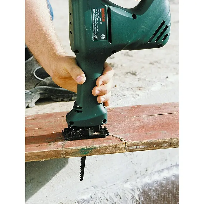 Wolfcraft Säbelsägeblatt - Weichholz/Faserplatte, Länge: 150 mm - Eine grüne Bosch Säbelsäge wird verwendet, um ein Stück Holz zu schneiden, das auf einer Betonoberfläche liegt.