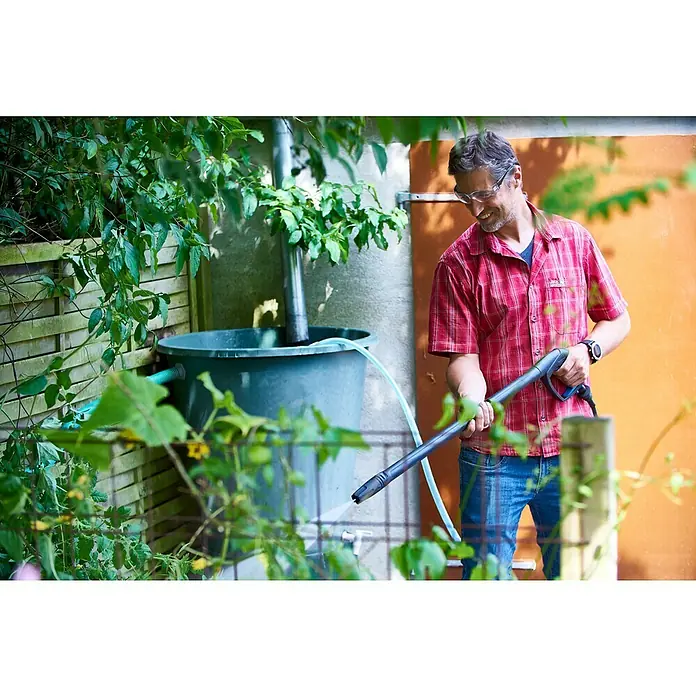 Nilfisk SaugschlauchLänge: 3 m - Ein Mann benutzt einen Hochdruckreiniger im Garten, um einen Behälter zu reinigen, der neben einem Zaun steht.