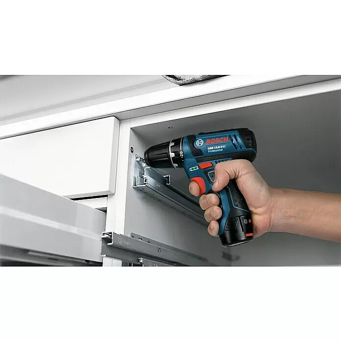 Bosch Professional Akku-Schlagbohrschrauber GSB 12V-15 - 12 V, 2 Akkus, 2 Ah - 4 Ah, 30 Nm, 2 Akkus + Ladegerät + 25-tlg. Bit-Set/14-tlg. Bohrer-Set + Tasche - Eine Hand hält einen blau-schwarzen Bosch Akku-Bohrschrauber und schraubt in eine Metallschiene bei der Schrankmontage.