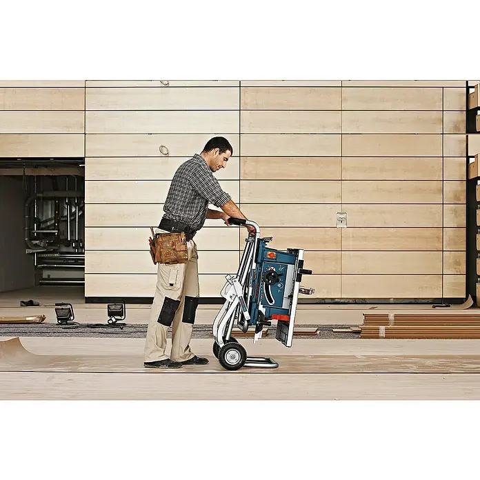 Bosch Professional Werkbank GTA 60 W - Arbeitshöhe: 622 mm, Belastbarkeit: 180 kg - Ein Handwerker transportiert eine tragbare Bosch Tischkreissäge auf einem Baustelle. Das Gerät ist kompakt und leicht zu transportieren.
