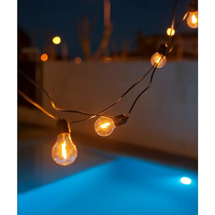 New Garden Guirnalda luminosa solar Allegra - 8,4 W, Largo: 8 m, LED, Blanco cálido, Negro, Número de bombillas: 10 ud. - Guirnalda de luces con bombillas de color blanco cálido colgando sobre una piscina que crea un ambiente acogedor de noche.