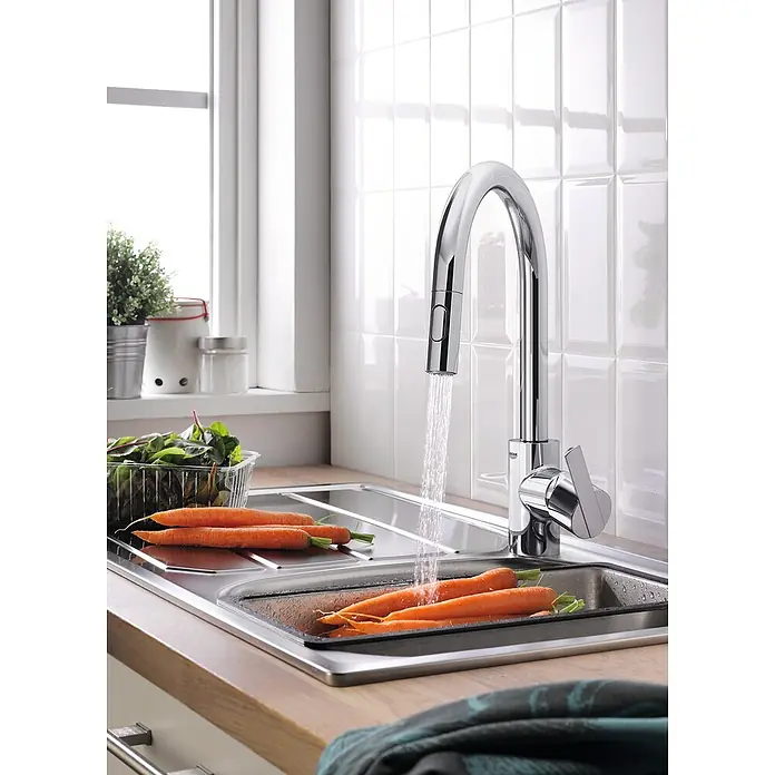 Grohe QuickFix Feel Grifo de cocina - Profundidad del grifo: 223 mm, Cromo, Brillante - Un elegante grifo de cocina cromado con agua corriente, zanahorias y lechuga que se están limpiando en un fregadero moderno.