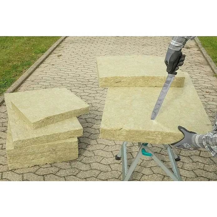 Wolfcraft Dämmstoffmesser - Klingenlänge: 305 mm - Ein Mann schneidet eine Platte aus Mineralwolle mit einem Messer auf einem Arbeitstisch, neben einem Stapel weiterer Platten.
