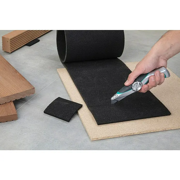 Wolfcraft Trapezmesser - Länge: 52 mm - Zuschneiden einer Dämmmatte mit einem Cuttermesser auf einer Holzunterlage, neben Holzplatten. Ideal für Bauprojekte.
