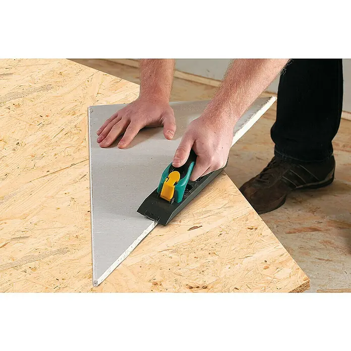 Wolfcraft Kantenhobel - Geeignet für: Gipskartonplatten - Ein Handwerker verwendet einen Kantenhobel mit grünem Griff und gelber Verriegelung, um eine Gipskartonplatte auf einer Arbeitsfläche zu bearbeiten.