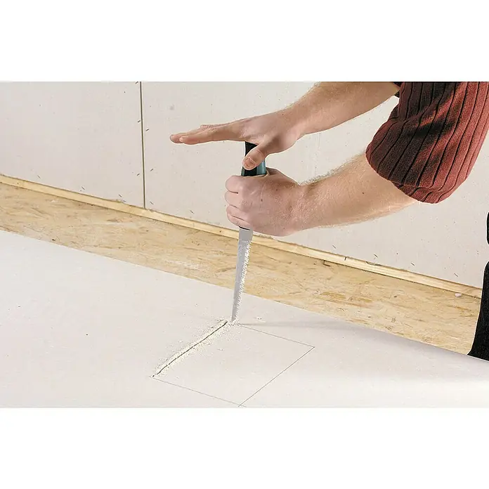 Wolfcraft Serrucho de calar para placas de yeso laminado - Apto para: Placas de yeso laminado - Un primer plano muestra a una persona usando una sierra de paneles de yeso para cortar un agujero cuadrado en una lámina de yeso blanca, con una mano que estabiliza el material.