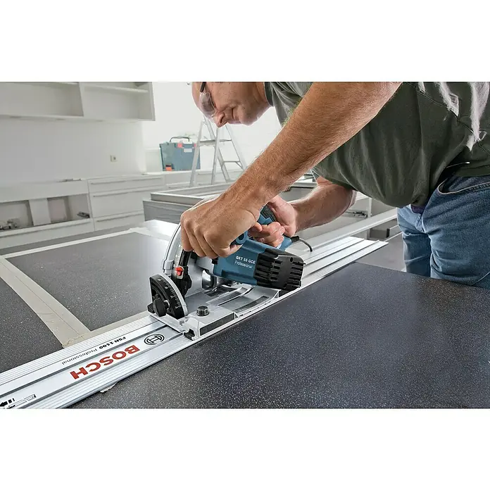 Bosch Professional Tauchsäge GKT 55 GCE - 1.400 W, Durchmesser Sägeblatt: 165 mm, Leerlaufdrehzahl: 6.250 U/min - Ein Mann schneidet mit einer Bosch GKT 55 GCE Professional Tauchsäge mit Führungsschiene FSN 1100 eine dunkle Arbeitsplatte zu.