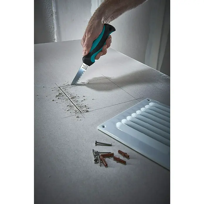 Wolfcraft Serrucho de calar para placas de yeso laminado - Apto para: Placas de yeso laminado - Un hombre está cortando un agujero en una placa de yeso con una sierra para paneles de yeso, junto a él hay rejillas de ventilación, tornillos y tacos.