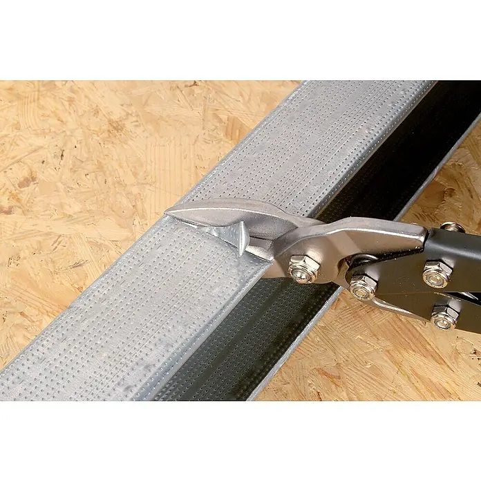 Wolfcraft Blechschere - Länge: 255 mm, Gerade - Blechschere schneidet ein Stück Metallprofil. Das Werkzeug ist silberfarben und hat schwarze Griffe. Die Oberfläche ist hellbraun.
