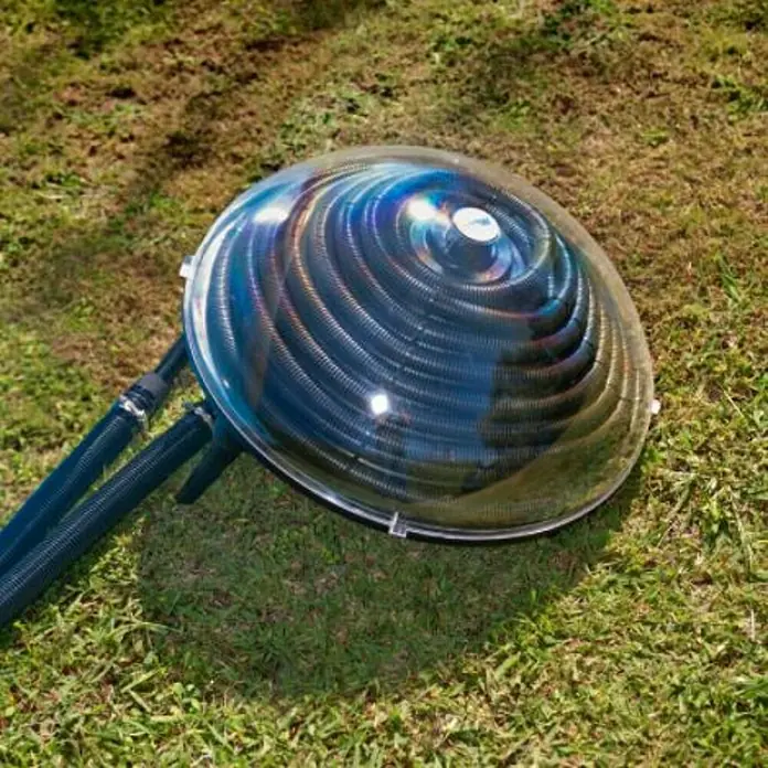 Gre Calentador Solar 90230 - L x An x Al: 57 x 57 x 25 cm, Polipropileno - Un primer plano de un calentador solar para piscinas situado sobre una superficie cubierta de hierba, que muestra su cúpula transparente que revela los tubos en espiral en su interior.