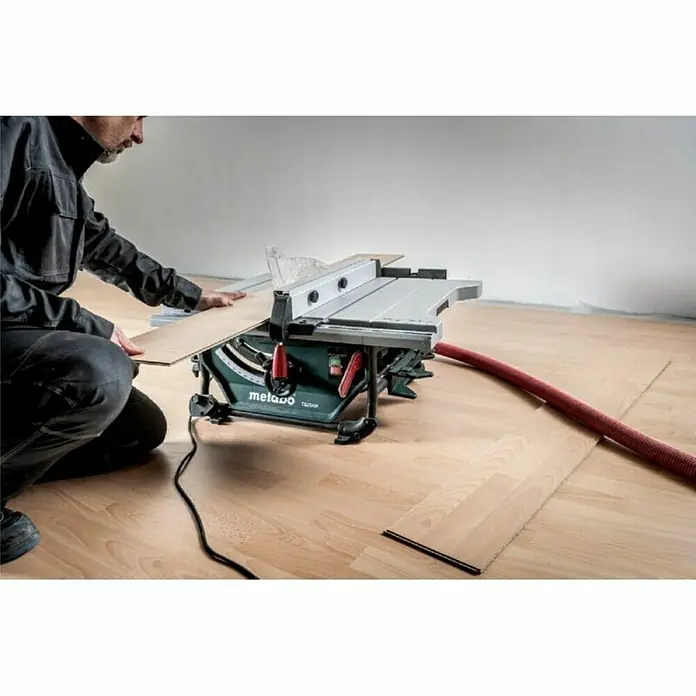 Metabo Tischkreissäge TS 254 M - 1.500 W, Durchmesser Sägeblatt: 254 mm, Schnitttiefe bei 90 °: 80 mm - Ein Handwerker benutzt eine Metabo Tischkreissäge zum Schneiden von Holzplatten. Das Werkzeug steht auf einem hellen Holzboden und ist an einen Staubsauger angeschlossen.