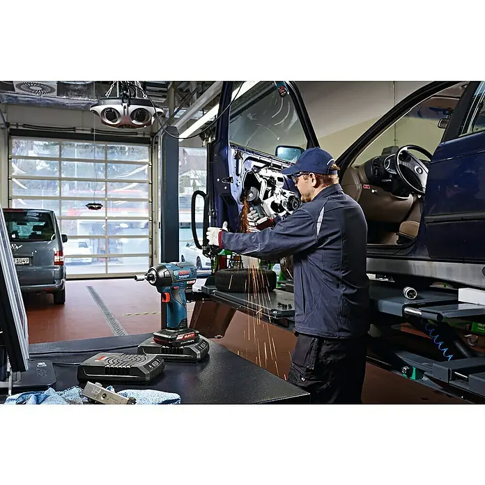 Bosch Professional Akku-Winkelschleifer GWS 12V-76 - 18 V, 2 Akkus, 2 Ah, Durchmesser Scheibe: 76 mm - Bild eines Bosch Professional Akku-Schlagschraubers mit Zubehör in einer Werkstatt, während ein Mechaniker an einem Auto arbeitet.
