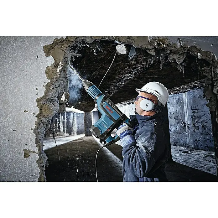 Bosch Professional Kombihammer GBH 12-52DV - 1.700 W, 19 J, SDS-Max-Aufnahme - Ein Bauarbeiter mit Schutzhelm und Gehörschutz arbeitet mit einem Bosch Abbruchhammer an einer Betonwand, um eine Öffnung zu schaffen.