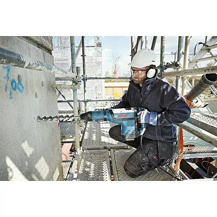 Bosch Professional Kombihammer GBH 12-52DV - 1.700 W, 19 J, SDS-Max-Aufnahme - Ein Mann auf Gerüst bohrt mit blauem Bosch Professional Bohrhammer in Betonwand auf Baustelle.