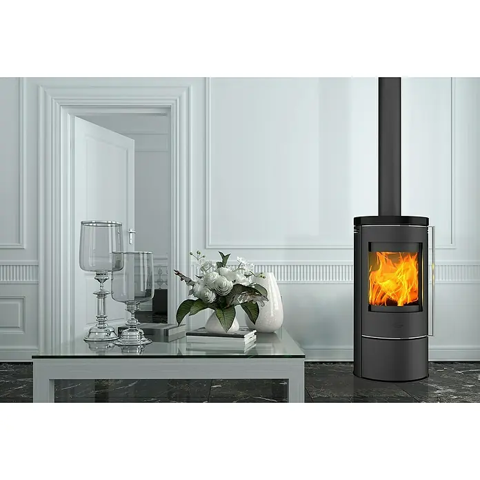 Fireplace Kaminofen Rondale - 5,5 kW, Raumheizvermögen: 90 m³, Material Verkleidung: Keramik, Schwarz - Elegantes Wohnzimmer mit einem stilvollen Kaminofen, der Wärme und Ambiente ausstrahlt, ergänzt durch dekorative Elemente auf einem Glastisch.