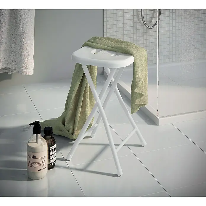 Gedy Taburete Levante - 305 x 275 x 465 cm, Plástico, Blanco - Un taburete de baño blanco y plegable con una toalla verde encima. Dos productos están en el suelo.