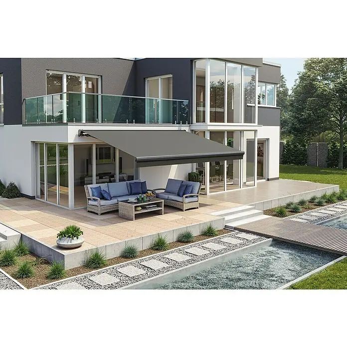 Solid Elements Teilhülsenmarkise Solid 320925Dunkelgrau strukturiert, Breite: 3,5 m, Ausfall: 3 m - Moderne Hausfassade mit grauer Markise über der Terrasse. Bequeme Gartenmöbel und ein idyllischer Teich laden zum Verweilen ein.