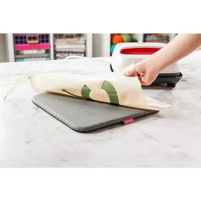 Cricut Hitzepress Schutzmatte EasyPress-Matte - Graubraun, L x B: 30 x 30 cm, Passend für: Cricut EasyPress® Transferpresse - Nahaufnahme eines Cricut-Presskissens mit einem leichten Canvas-Beutel, der mit einem grünen Design beklebt wird, perfekt für Bastelprojekte.