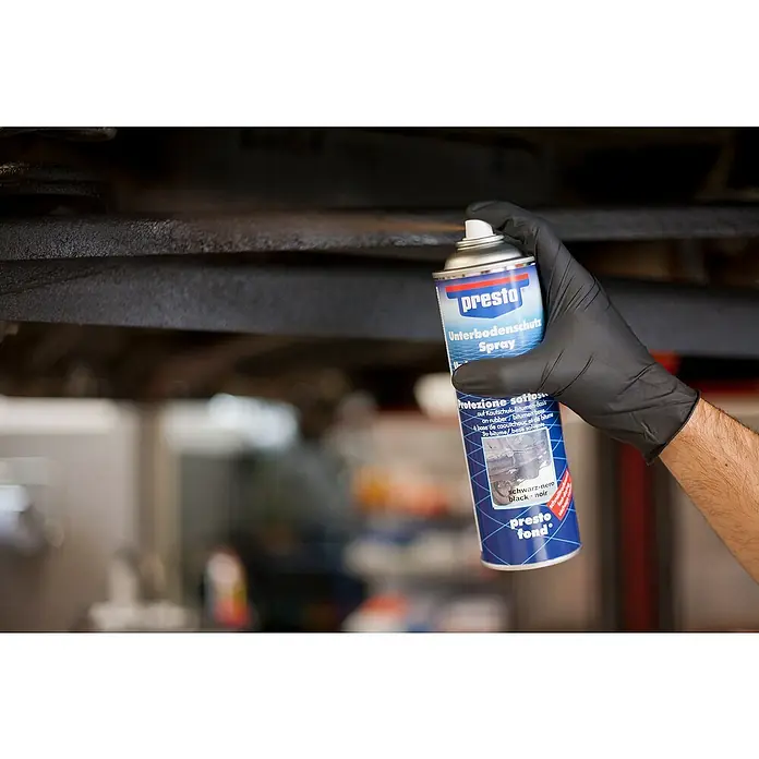 Presto Unterbodenschutz - 500 ml, Sprühdose - Ein dunkler Unterbodenschutz-Spray von Presto wird von einer Hand mit schwarzem Handschuh gehalten, um das Auto zu schützen.