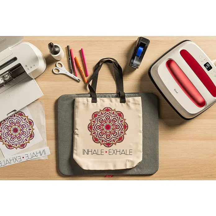 Cricut Stoffbeutel Large für Infusible Ink - Beige/Schwarz, L x B: 48 x 35,5 cm, 100 % Polyester - Nahaufnahme einer Cricut EasyPress 2 Heißpresse, einem Cricut Maker Schneideplotter und einer Tragetasche mit Mandala-Design.