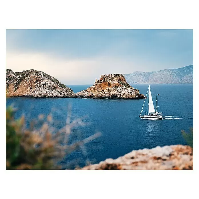 Póster Mallorca - Velero Santa Ponsa, An x Al: 80 x 60 cm - Velero blanco con velas izadas, navegando en agua azul junto a islas rocosas y una costa montañosa.