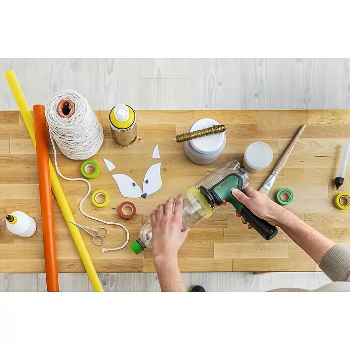 Bosch Akku-Winkelschleifer Easycut&Grind - 7,2 V, 1 Akku - Hände schneiden eine klare Plastikflasche mit einem grünen und schwarzen Bosch-Werkzeug auf einem Holztisch, umgeben von Bastelmaterial.