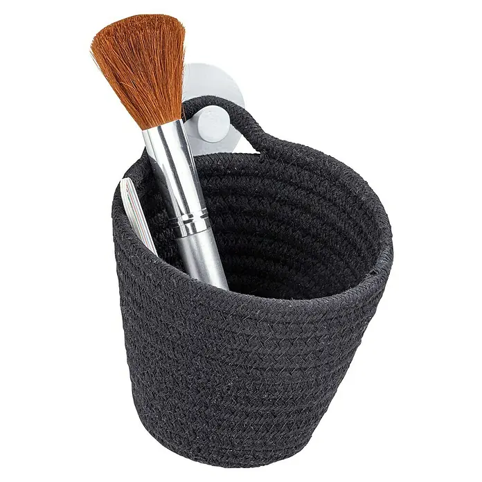 Wenko Cesto Soria - 14,5 x 12,5 x 12 cm, Poliéster, Negro - Primer plano de un recipiente de almacenamiento tejido negro con una brocha de maquillaje y una lima de uñas, montado en un soporte de pared.
