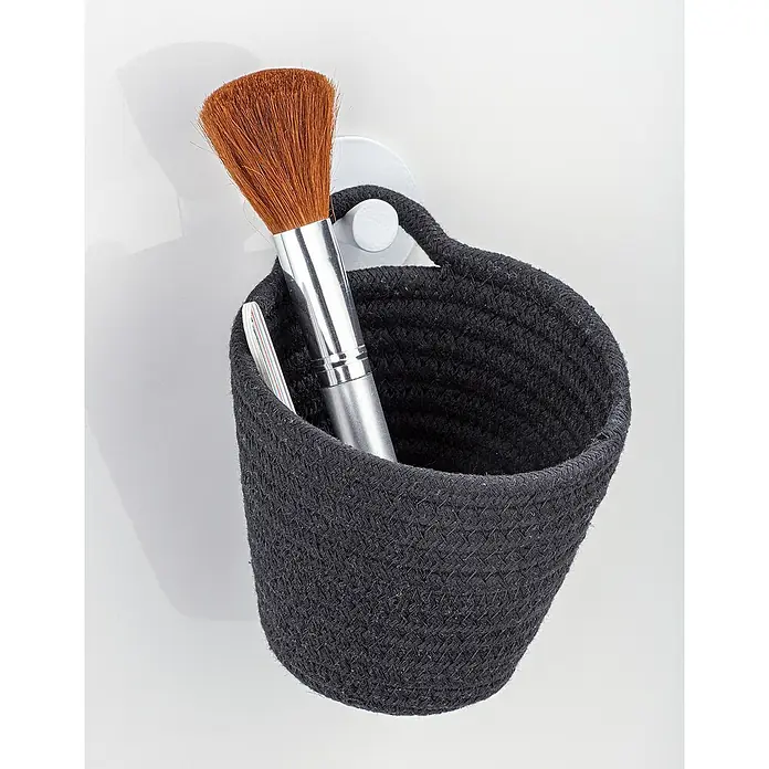 Wenko Ablagekorb Soria - 14,5 x 12,5 x 12 cm, Polyester, Schwarz - Eine Nahaufnahme eines schwarzen geflochtenen Korbes mit Kosmetikpinsel, der an einer weißen Wand hängt, ideal zur Aufbewahrung und Dekoration.