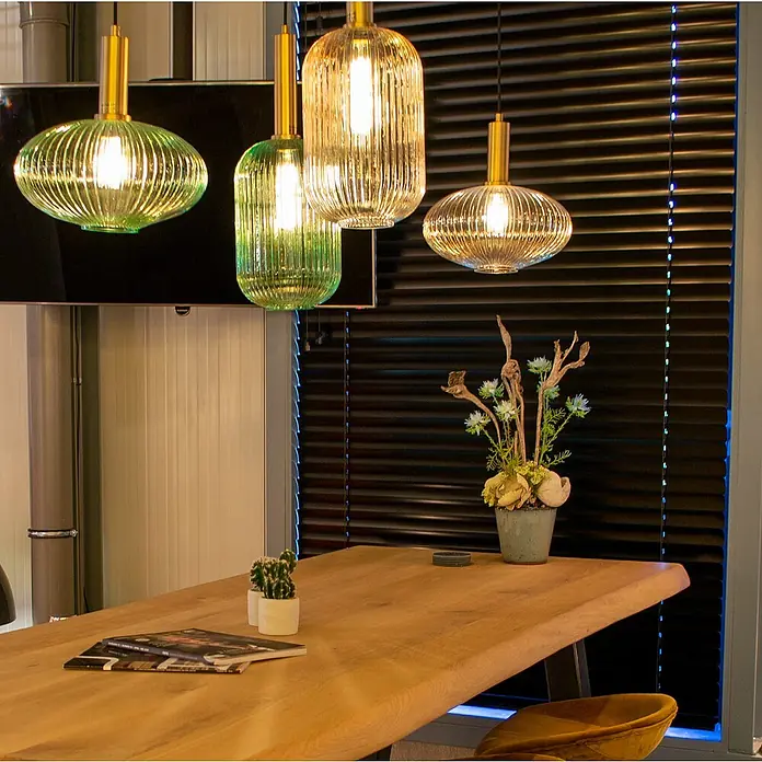 Lucide Maloto Pendelleuchte - 40 W, L x B x H: 150 x 20 x 150 cm, Bernstein/ Gold, E27 - Diese Aufnahme zeigt dekorative Lampen in Grün- und Goldtönen über einem Holztisch, die eine warme Atmosphäre erzeugen.