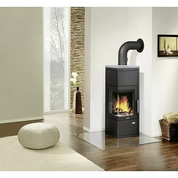Justus Kaminofen Diego wärmePLUS - 6 kW, Raumheizvermögen: 115 m³, Material Verkleidung: Speckstein, Schwarz/Speckstein - Moderner schwarzer Kaminofen mit Eckscheibe, der ein warmes Feuer zeigt, in einem zeitgenössischen Wohnzimmer.