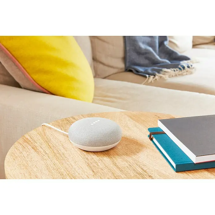 Google Nest Sprachgesteuerter Lautsprecher Mini - Kreide, Netzbetrieben, Kabellänge: 1,5 m - Ein Google Nest Mini Smart Speaker in grau auf einem Holztisch neben zwei Büchern.