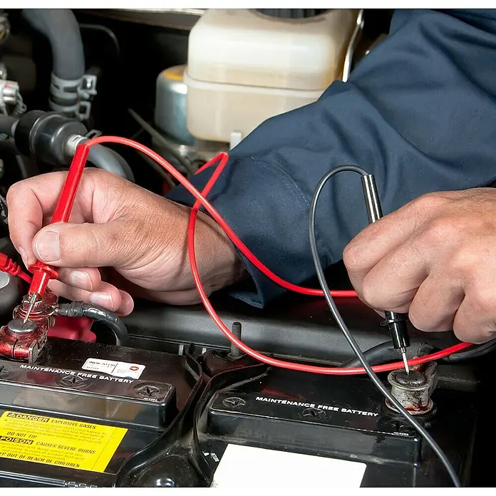 Laserliner Analog-Multimeter Home - 12 V - 300 V - Ein Mechaniker prüft die Spannung einer wartungsfreien Autobatterie mit einem roten und einem grauen Kabel.