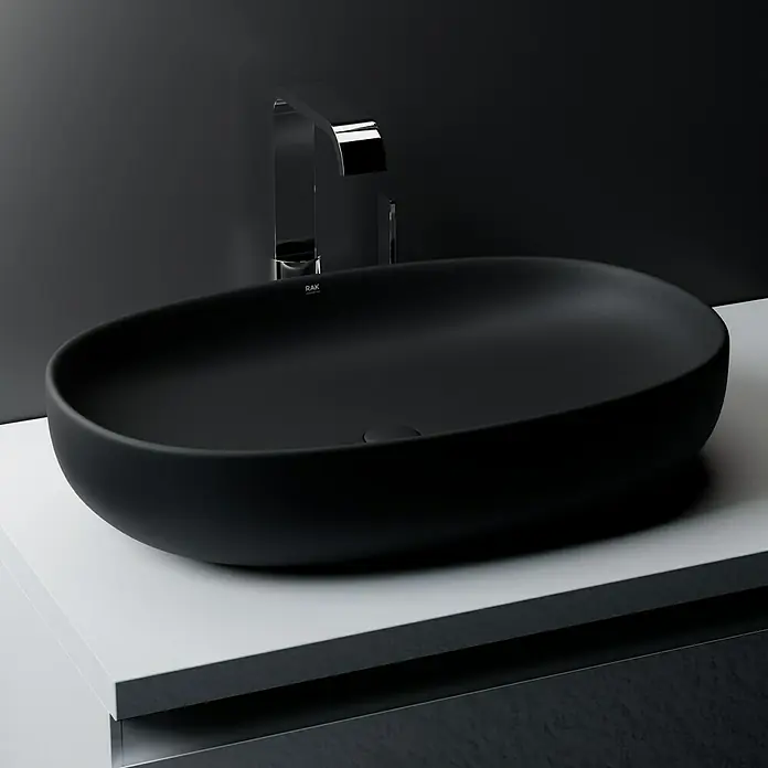 RAK Ceramics Feeling Ablaufventil - 1 ¼″, Schwarz, Mit Druckknopf - Schwarzes, ovales Aufsatzwaschbecken von RAK Ceramics auf einer weißen Oberfläche mit einem modernen, verchromten Wasserhahn.